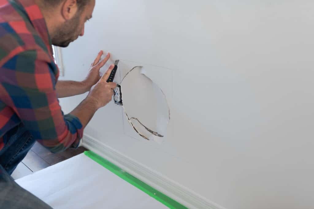 Handy Hive Pros technician repairing drywall, carefully cutting a damaged section to replace it with a seamless patch. Expert drywall repair services in Tampa, FL.