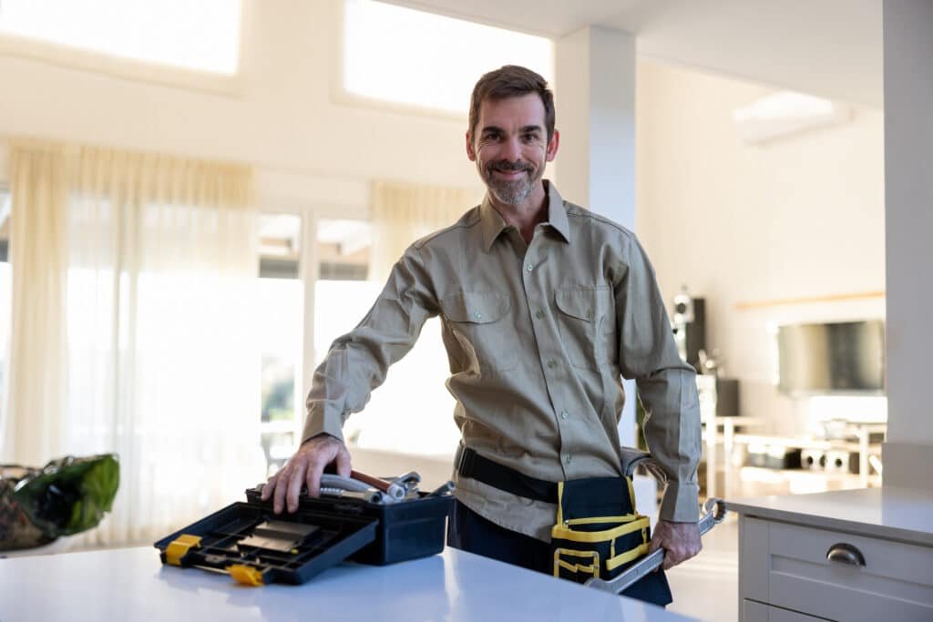 Smiling Handy Hive Pros technician standing in a modern home with a toolset, ready to assist with home repairs and maintenance in Tampa, FL.