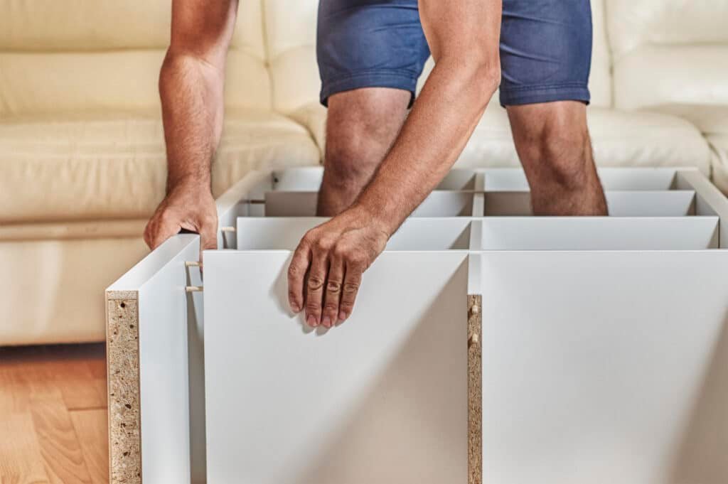 Handy Hive Pros technician assembling a white shelving unit in a modern living room. Expert furniture assembly services in Tampa, FL.