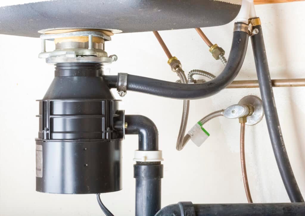 Close-up view of an under-sink garbage disposal unit, installed with connected pipes and plumbing by Handy Hive Pros.