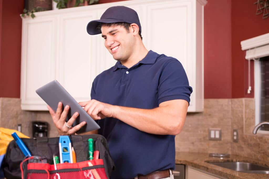 Handy Hive Pros handyman in uniform using a digital tablet for scheduling and service updates in a customer's home kitchen.