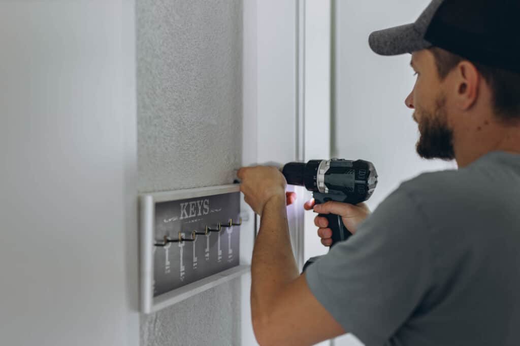 Professional handyman installing a key holder on a wall using a power drill – Handy Hive Pros home repair services.